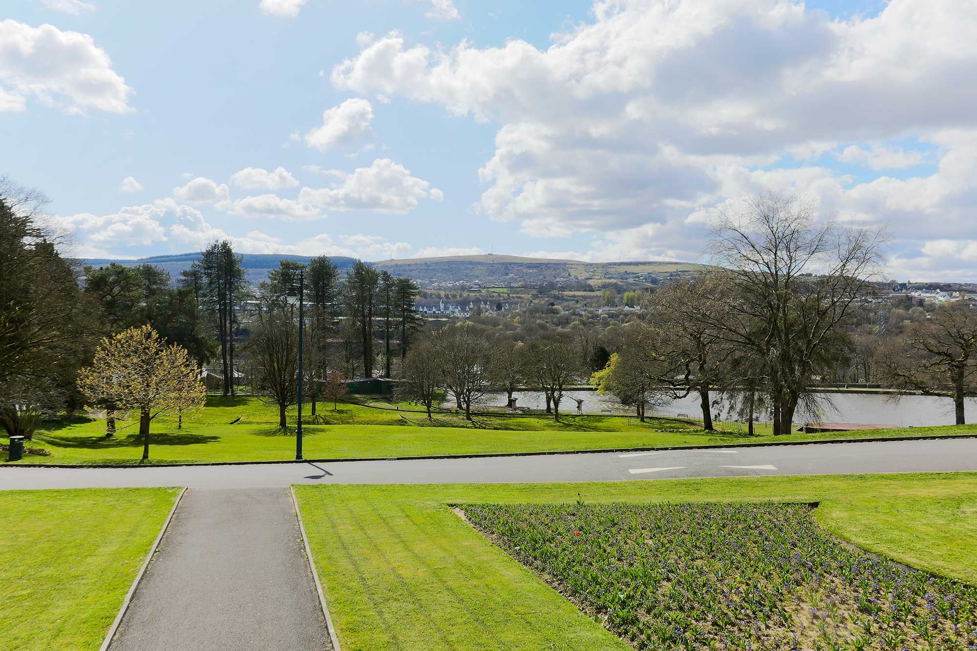 View of Cyfarthfa park with lawns and trees, with hills in the distance.jpg